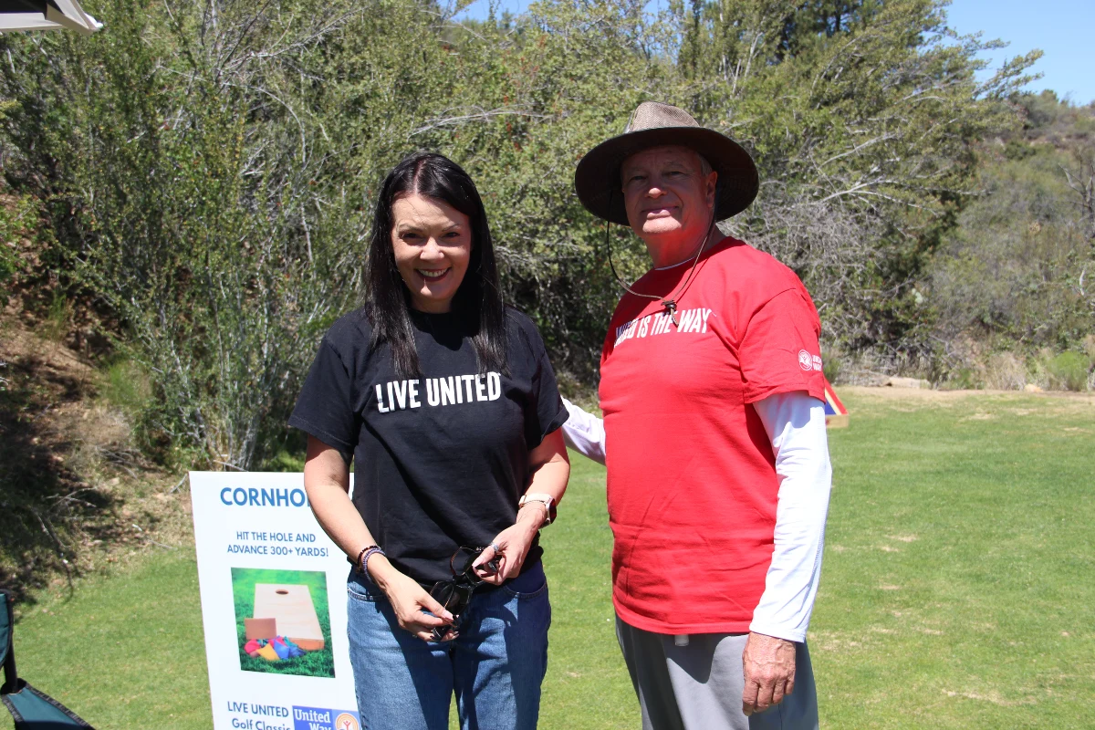 United Way volunteers pose beside the cornhole challenge station at the golf tournament